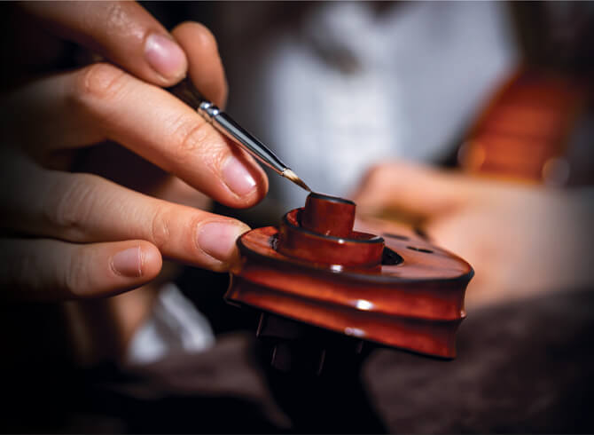 Close-up of hands painting a violin’s tuning peg with a fine brush, showcasing craftsmanship of top real estate builders in Mumbai 
